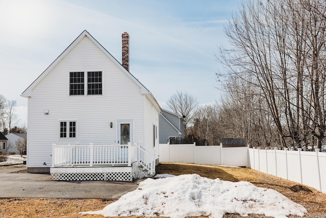 rear view of house featuring a deck, fence, and a chimney