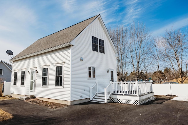 rear view of house with driveway, a deck, and fence