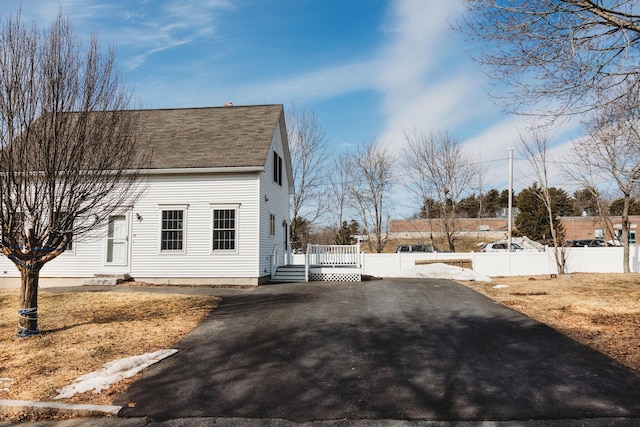 view of side of property with a wooden deck, fence, driveway, and a shingled roof