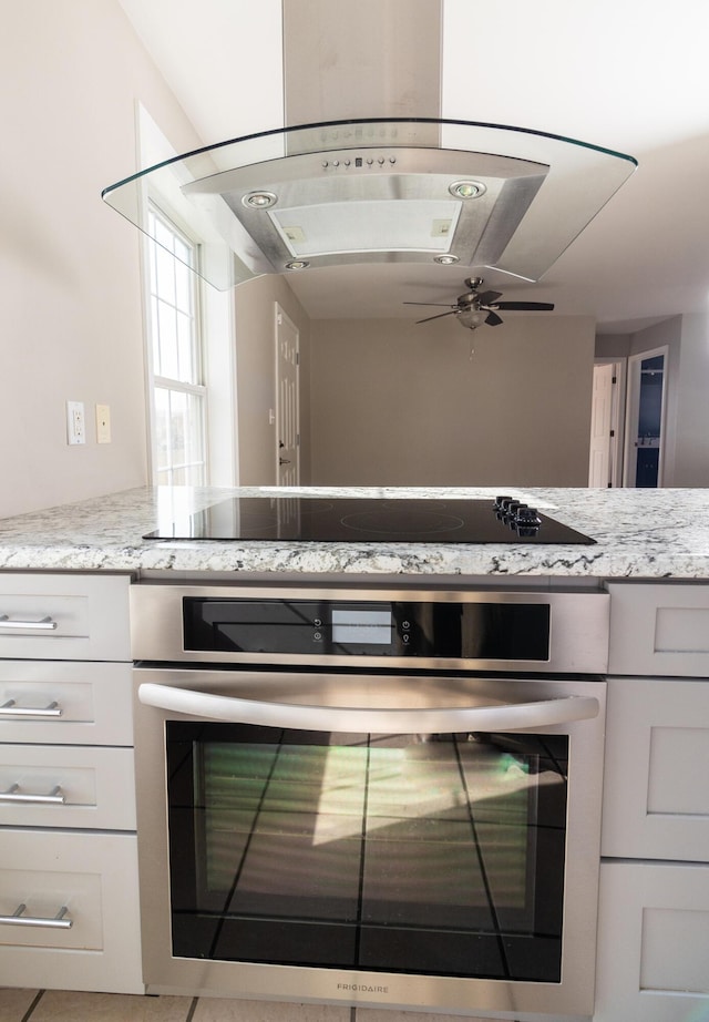 kitchen with oven, ceiling fan, light stone countertops, white cabinetry, and black electric cooktop