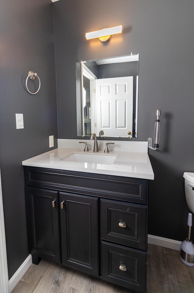 bathroom with vanity, toilet, wood finished floors, and baseboards