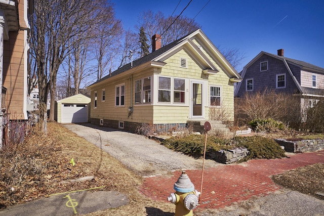 view of front facade with aphalt driveway, a detached garage, an outbuilding, and a chimney