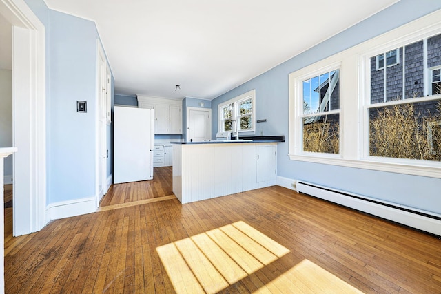 kitchen with a baseboard heating unit, dark countertops, freestanding refrigerator, wood-type flooring, and a peninsula