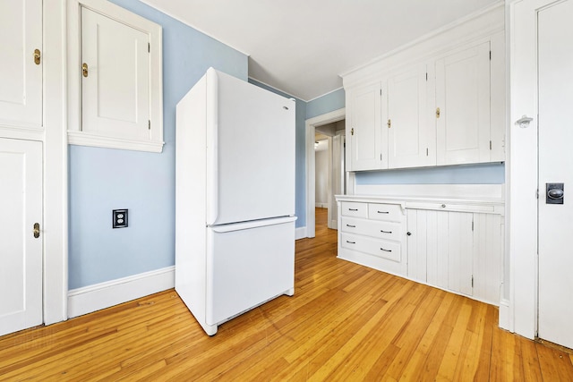 kitchen with white cabinets, light wood-type flooring, freestanding refrigerator, and light countertops