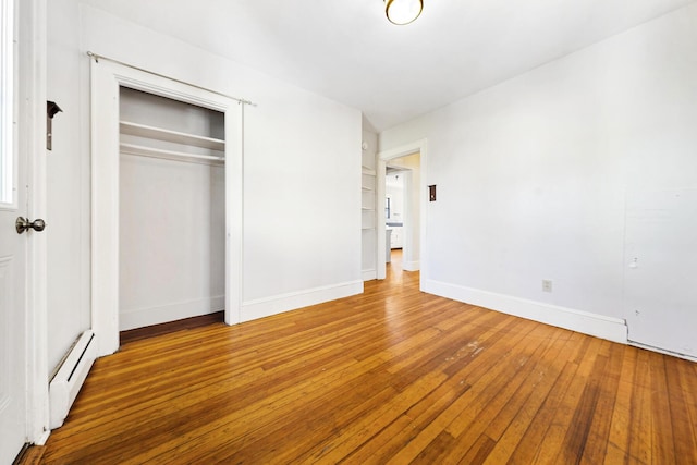 unfurnished bedroom featuring a closet, a baseboard heating unit, baseboards, and hardwood / wood-style flooring