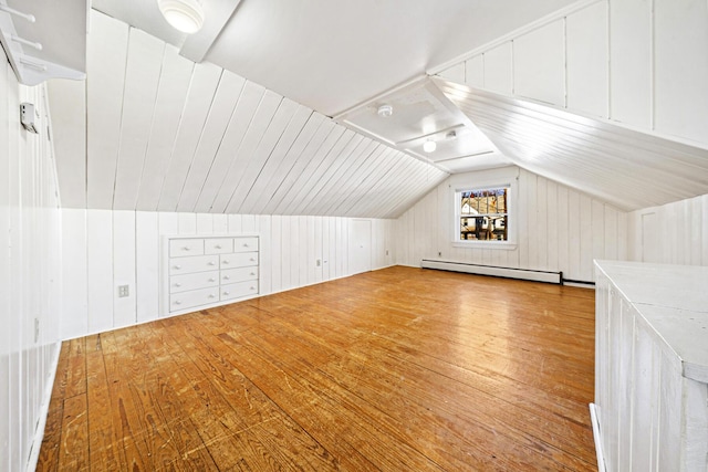 additional living space featuring a baseboard heating unit, vaulted ceiling, wooden walls, and hardwood / wood-style floors