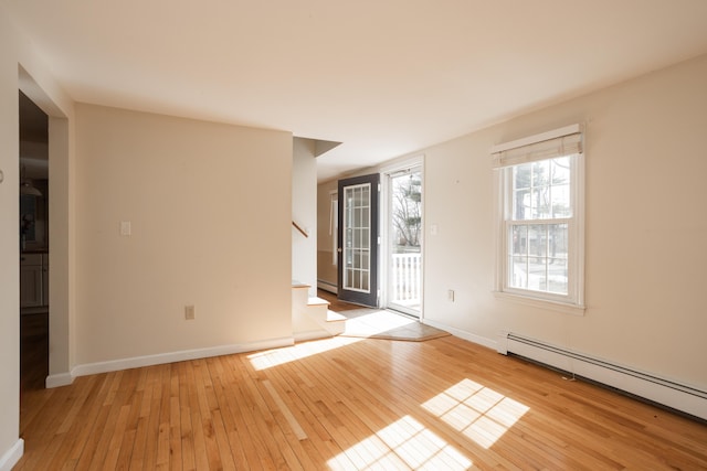 spare room with stairway, baseboards, light wood finished floors, and a baseboard radiator