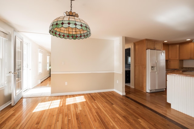 unfurnished dining area with light wood-style flooring, baseboards, and a baseboard radiator