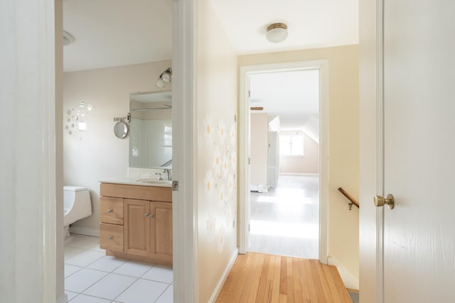 hall featuring a sink, baseboards, and light wood-style floors