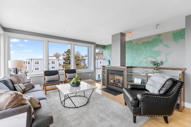 living area featuring baseboards, a fireplace with flush hearth, and wood finished floors