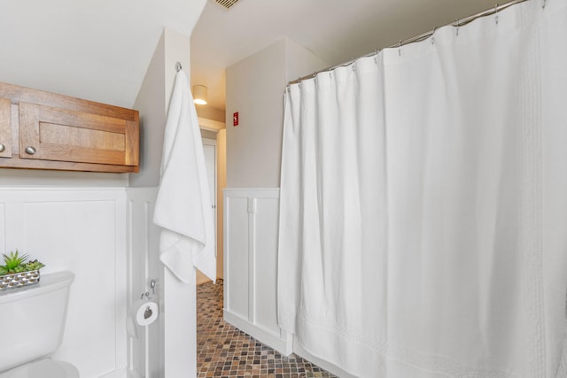 bathroom with a wainscoted wall, toilet, a decorative wall, and visible vents