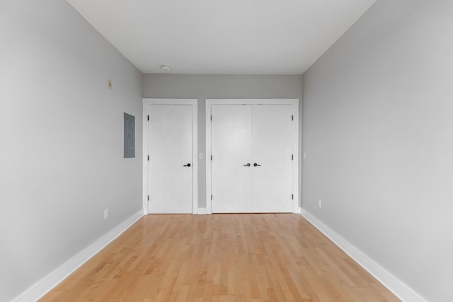 unfurnished bedroom featuring electric panel, light wood-type flooring, and baseboards