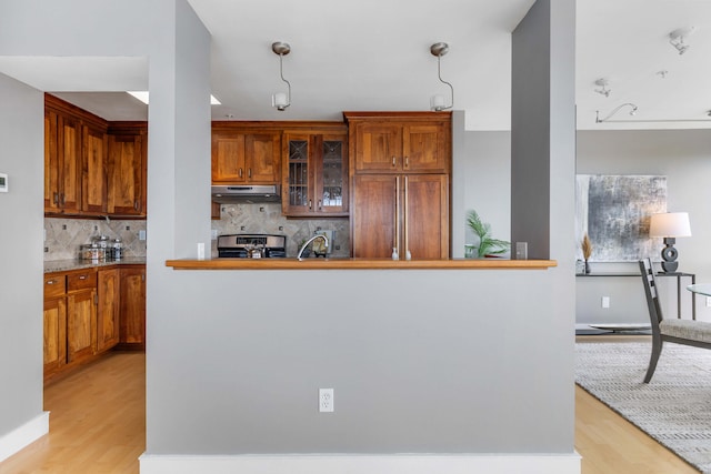 kitchen featuring under cabinet range hood, paneled built in fridge, stainless steel electric range, light wood finished floors, and decorative backsplash