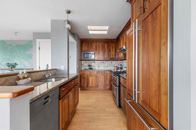 kitchen featuring a sink, under cabinet range hood, tasteful backsplash, appliances with stainless steel finishes, and a skylight