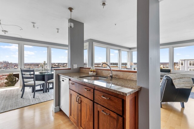 kitchen with light wood-style flooring, a sink, stone countertops, brown cabinetry, and dishwasher