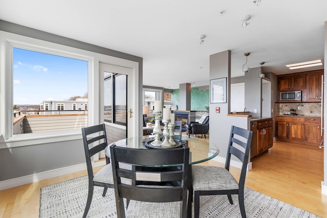 dining area featuring light wood-type flooring, baseboards, and a glass covered fireplace