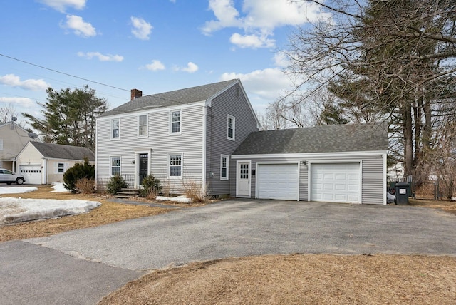 colonial inspired home featuring aphalt driveway, a chimney, an attached garage, and a shingled roof