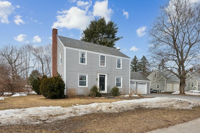 colonial house with aphalt driveway, a chimney, a garage, and a shingled roof