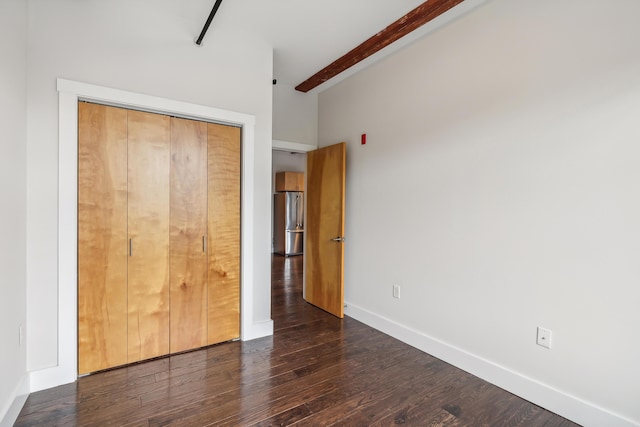 unfurnished bedroom with wood finished floors, baseboards, beam ceiling, freestanding refrigerator, and a closet