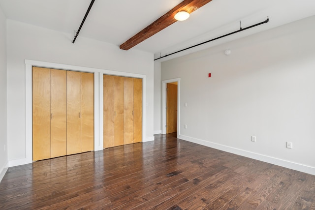 unfurnished bedroom with baseboards, beam ceiling, two closets, and wood finished floors