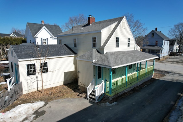 back of house featuring a chimney, a porch, a shingled roof, and fence