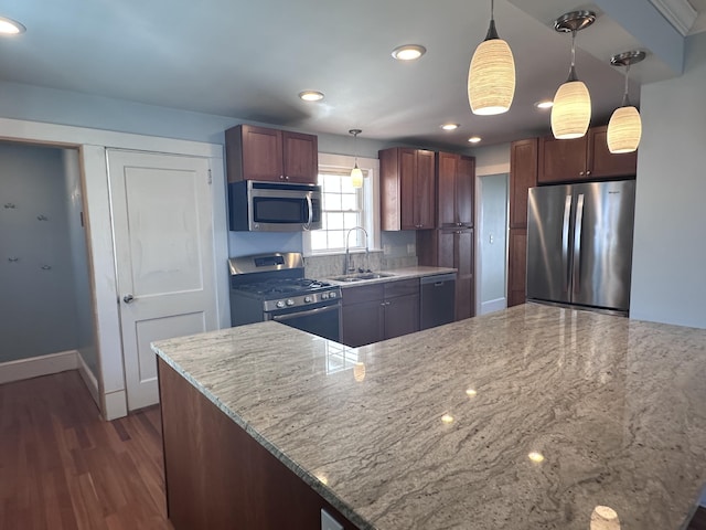 kitchen featuring a sink, decorative light fixtures, light stone counters, appliances with stainless steel finishes, and dark wood-style flooring