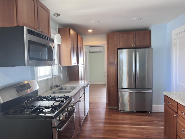 kitchen with a sink, light stone countertops, a wall mounted air conditioner, stainless steel appliances, and dark wood-style flooring