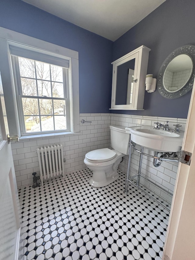 bathroom with radiator, a sink, wainscoting, tile walls, and toilet