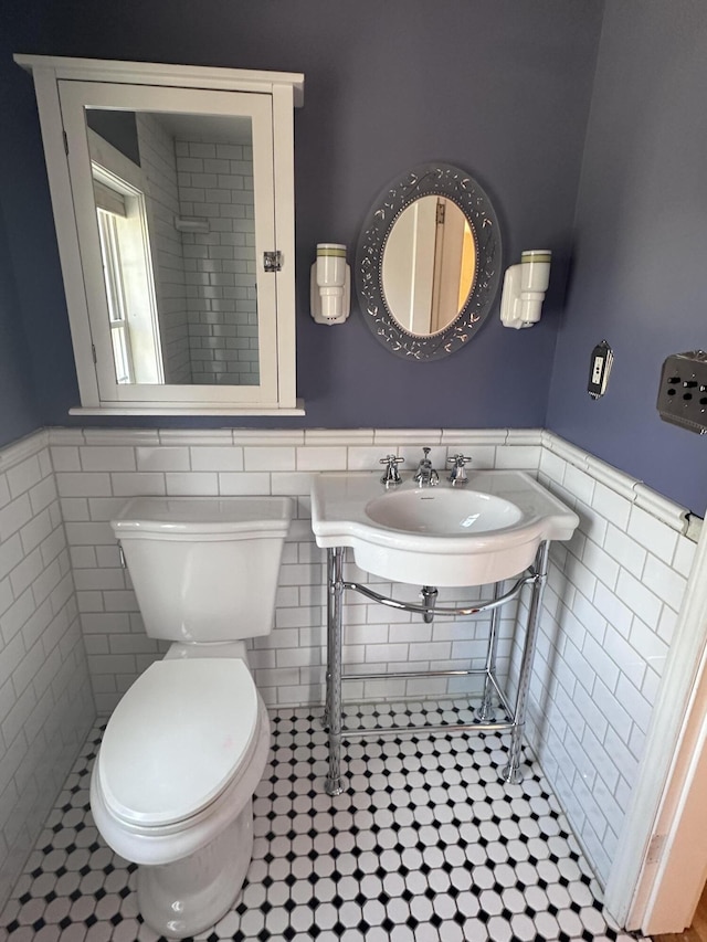 bathroom featuring a sink, toilet, tile walls, and wainscoting