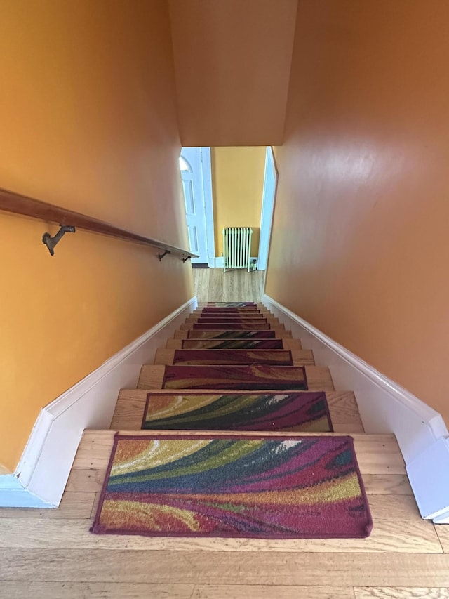 staircase with radiator, baseboards, a towering ceiling, and wood finished floors