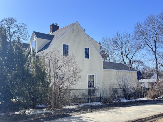 view of home's exterior with fence, roof with shingles, and a chimney