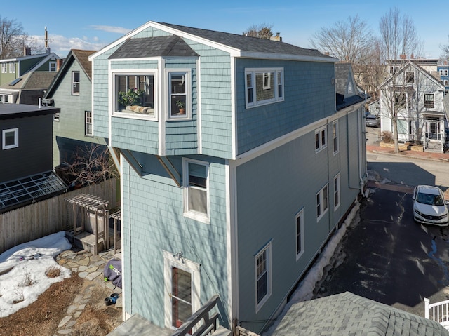 view of side of property with fence and roof with shingles