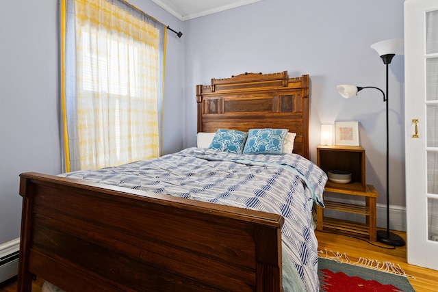 bedroom featuring crown molding, a baseboard heating unit, and wood finished floors