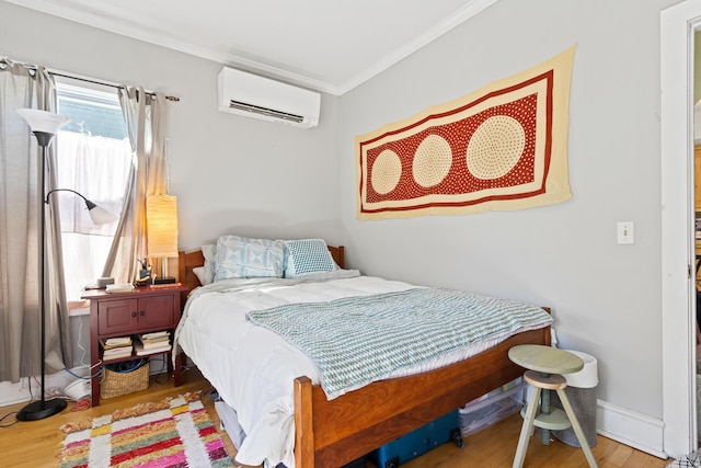 bedroom with a wall mounted air conditioner, baseboards, wood finished floors, and ornamental molding