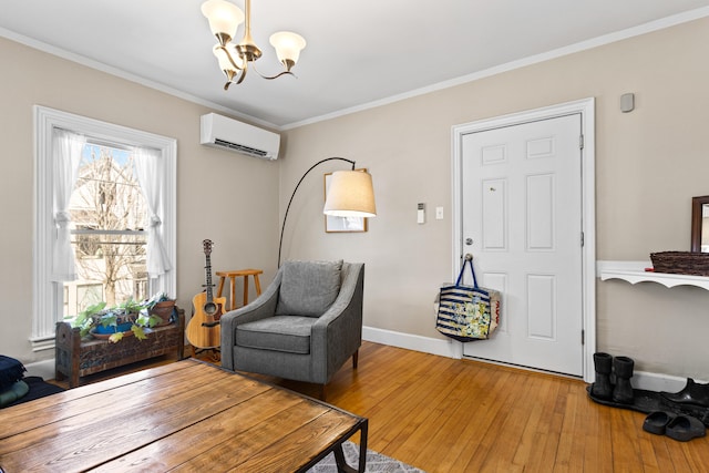 living area with an AC wall unit, hardwood / wood-style flooring, crown molding, baseboards, and a chandelier