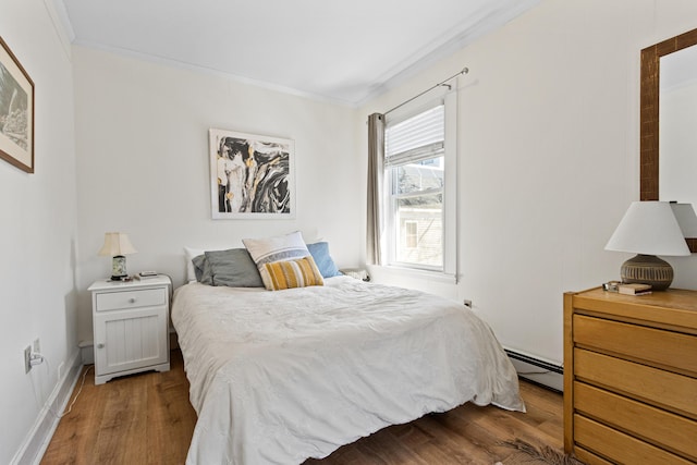 bedroom featuring wood finished floors, baseboard heating, and ornamental molding