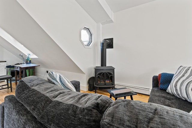 living room featuring vaulted ceiling, a wood stove, wood finished floors, and a baseboard radiator