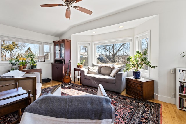 living area featuring lofted ceiling, light wood-style flooring, baseboards, and a wealth of natural light