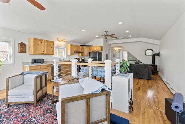 living room featuring light wood-type flooring, a baseboard heating unit, lofted ceiling, and a ceiling fan