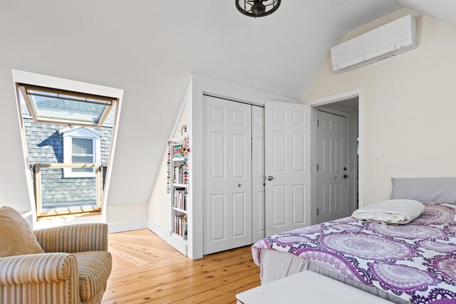 bedroom with lofted ceiling with skylight, light wood finished floors, a wall mounted air conditioner, and a closet