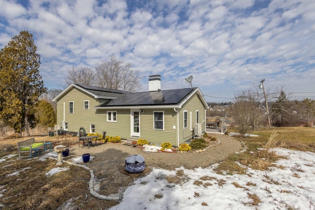 back of house with roof mounted solar panels, entry steps, and a chimney