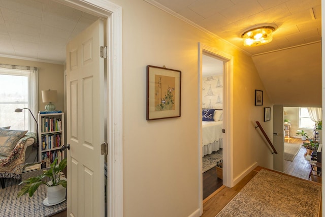 corridor with an upstairs landing, light wood-style flooring, crown molding, baseboards, and vaulted ceiling