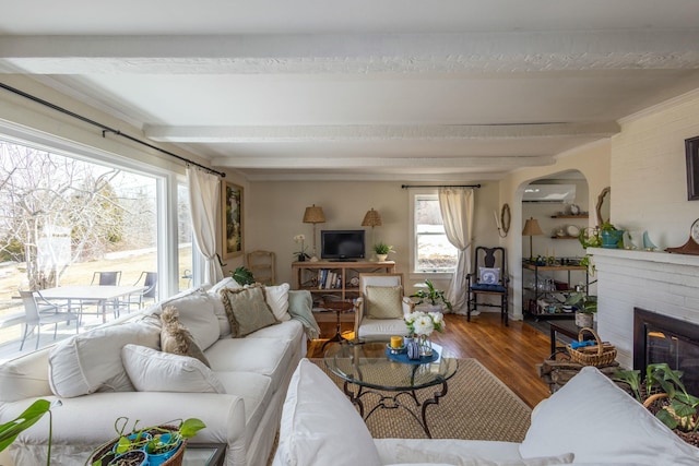 living room featuring beamed ceiling, a wall mounted AC, wood finished floors, arched walkways, and a fireplace