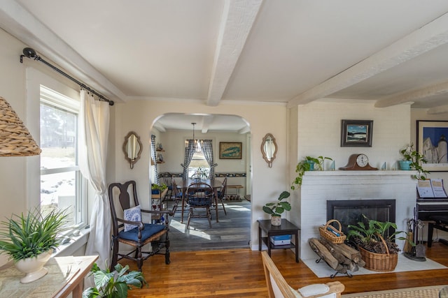 living room with arched walkways, beam ceiling, a fireplace, and wood finished floors