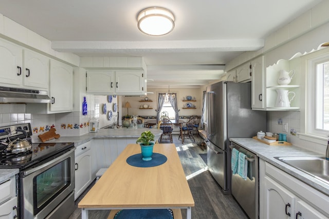 kitchen featuring under cabinet range hood, beamed ceiling, tasteful backsplash, and appliances with stainless steel finishes