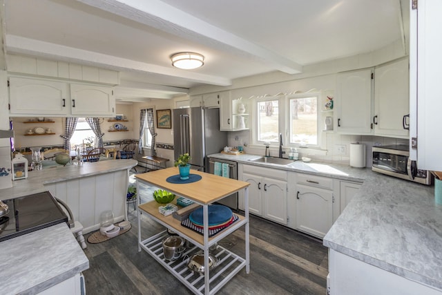 kitchen featuring beam ceiling, a sink, stainless steel appliances, dark wood-type flooring, and white cabinets