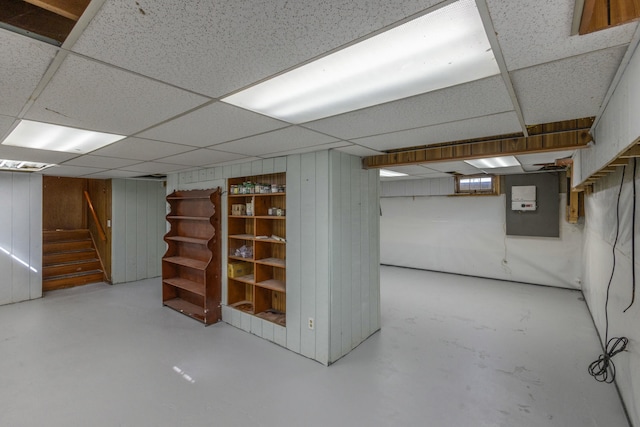 finished basement with stairway, wooden walls, and a paneled ceiling