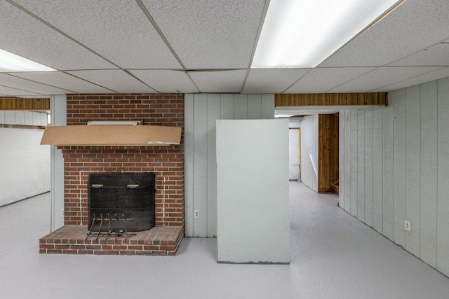 finished basement featuring a brick fireplace, wooden walls, and a drop ceiling