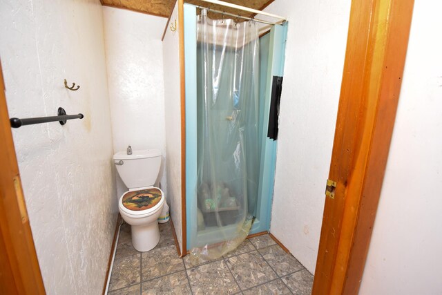 bathroom featuring a shower with shower curtain, toilet, and stone finish flooring