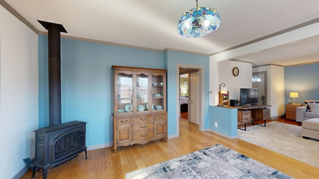 living area with baseboards, wood finished floors, a wood stove, and crown molding